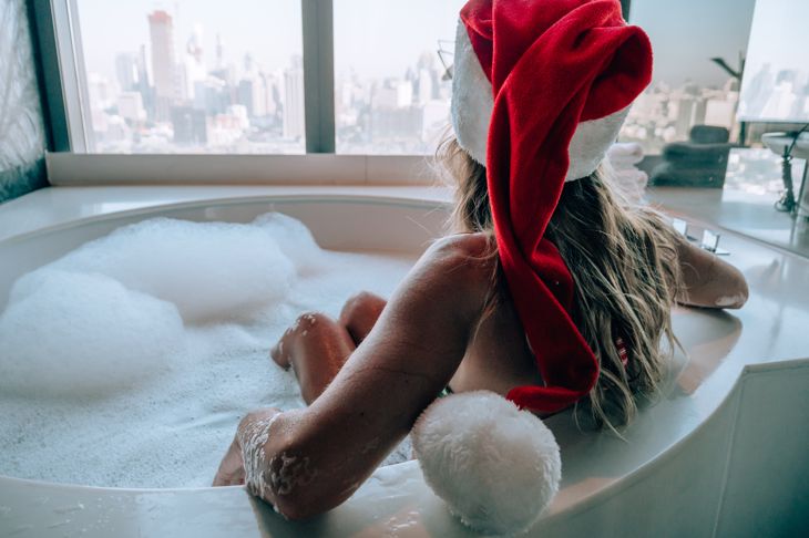 Young woman taking a bath wearing Santa hat, Christmas relaxation