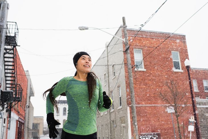 Happy young female runner in knitted hat running in snowy street