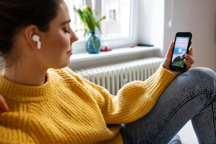Woman relaxing by listening to mindfulness music from smartphone app.  Caucasian woman wearing wireless earphones listen and feel the music while at home.