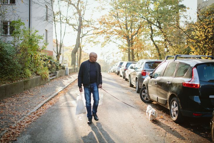 Full length of elderly man with shopping bag walking with dog on road in autumn