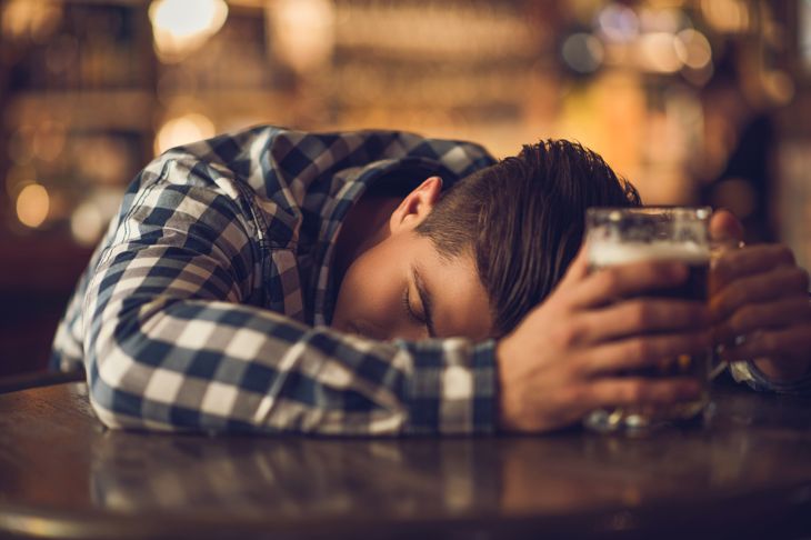 Drunk man sleeps in bar while holding a glass of beer