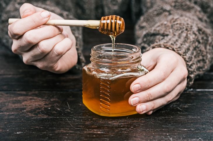 Human hands with opened small glass can of honey and dipper