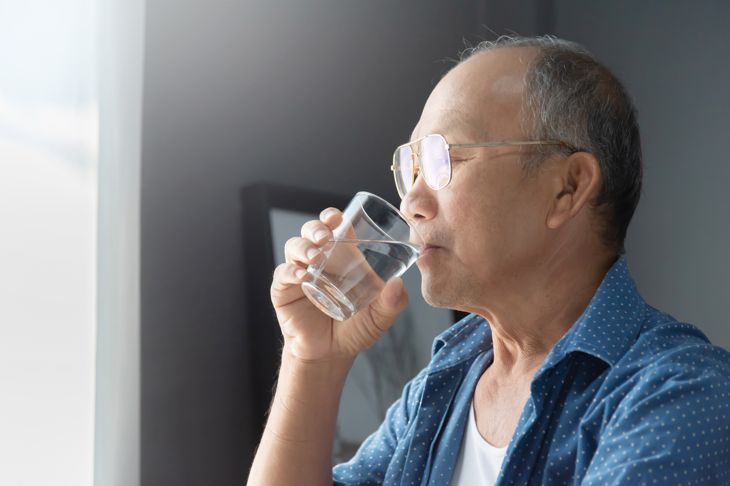 An elderly man drinking a glass of water