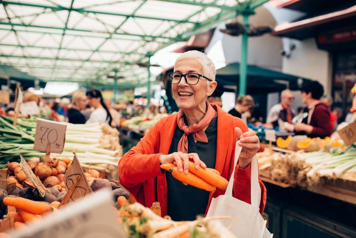 An elderly woman buying carrots in a marketplace