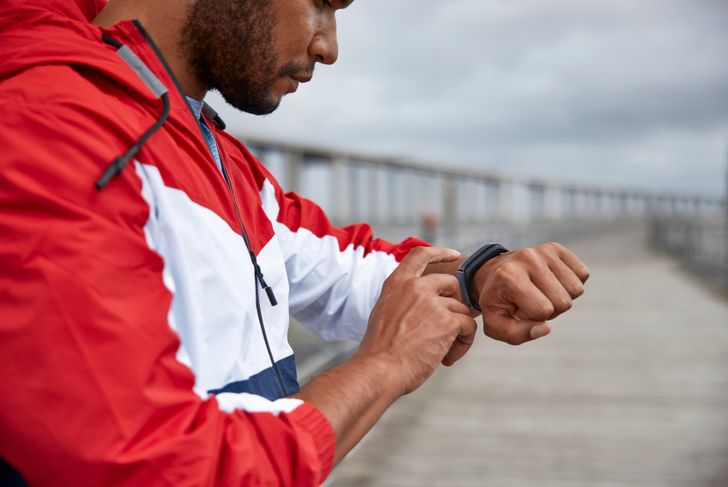 African-American man taps fitness tracker after crossing river bridge
