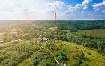 Telecommunication tower with  radio antennas and satellite dishes is installed on the rural on the green field with grass, bushes and trees. Concept of harmless of electromagnetic and microwav