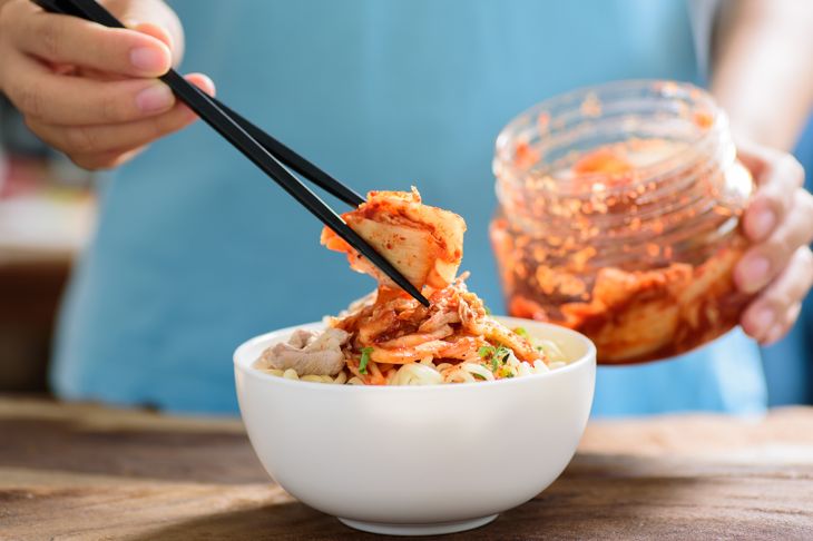 person putting kimchi on noodles