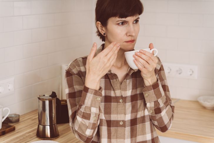 Woman sniffs the smell of coffee from the cup while preparing a drink in the kitchen in the morning