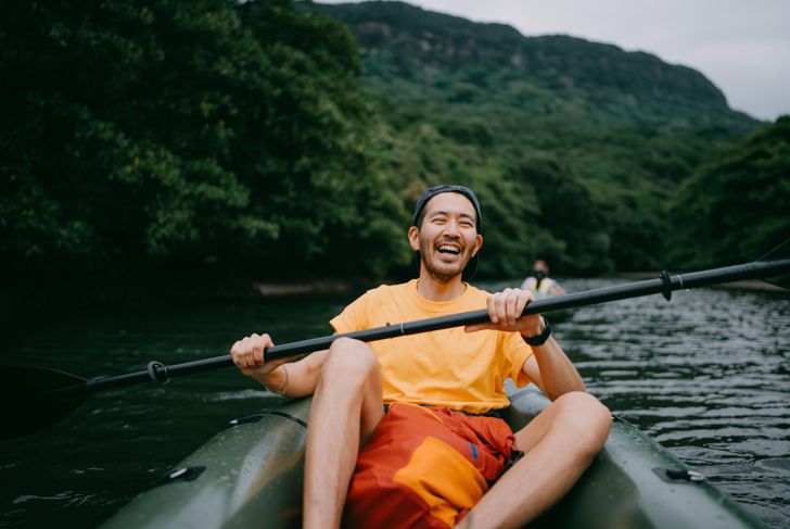 Man paddling kayak in mangrove river and laughing