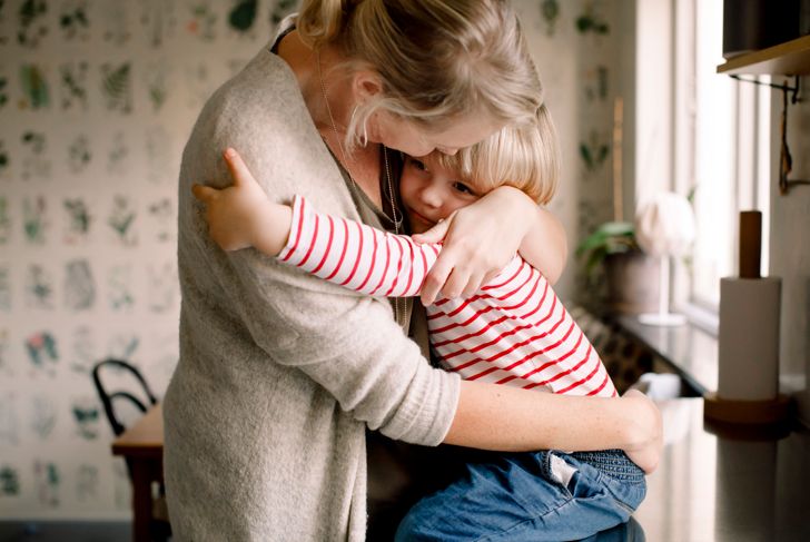 Loving daughter hugs mom while sitting on kitchen counter at home