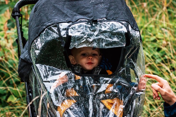 Little boy walking in pram with rain protection cover
