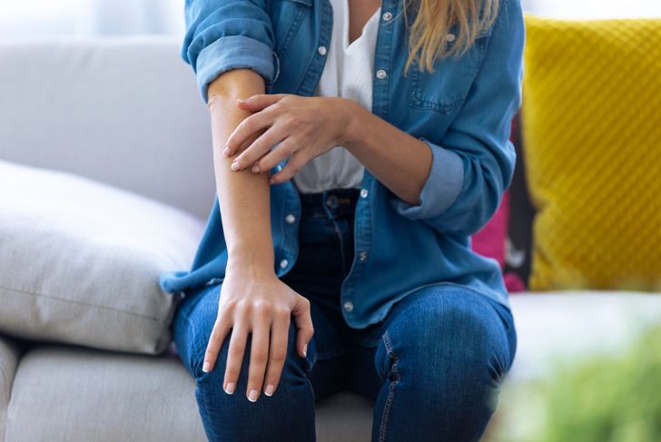 woman scratching her arm while sitting on the couch