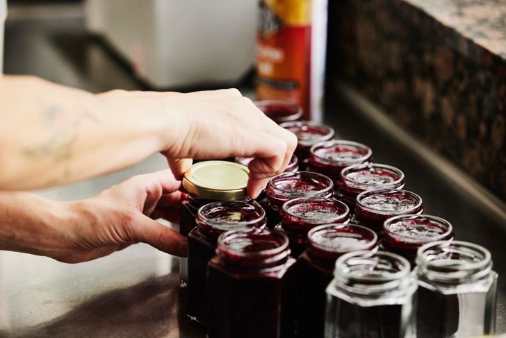 Female chef putting lids on jars with freshly made organic jam
