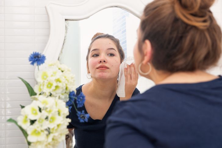woman looking in the mirror and wiping her face with wipes