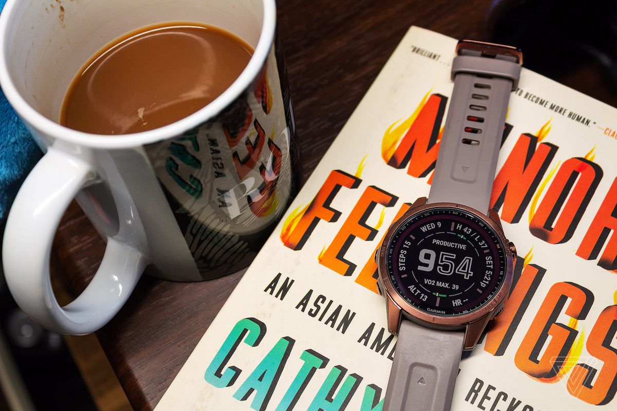 The Garmin Fenix ​​7S on top of a book and next to coffee.