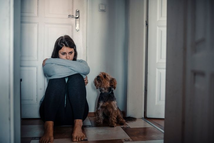Woman with mental health problems sits desperately on the floor and cries and her dog is next to her