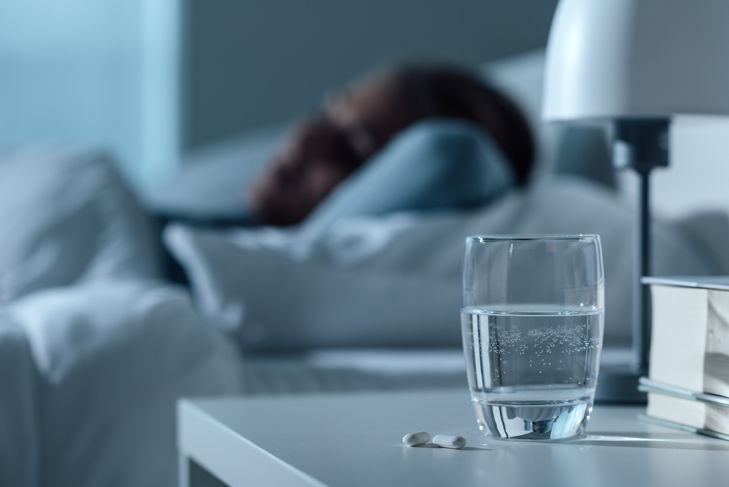 Woman sleeps in her bed at night, glass on water and pills in the foreground