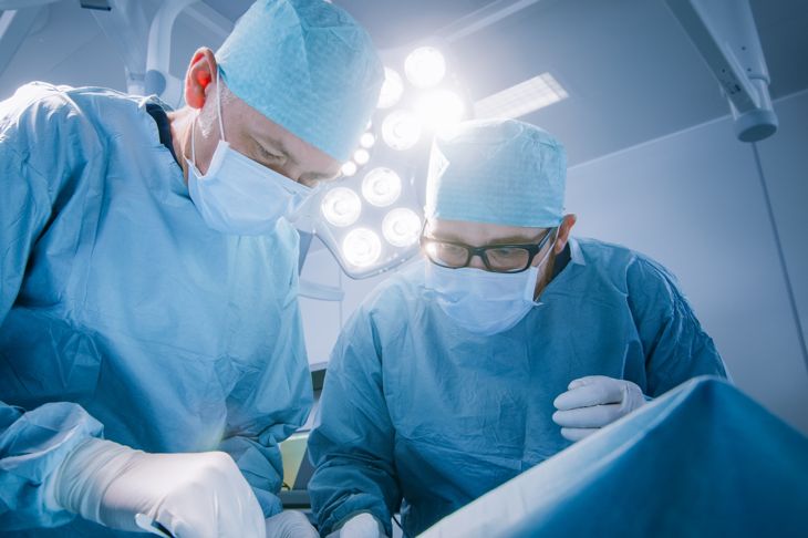 Low angle shot in operating room of two surgeons bending over patient with instruments during surgery procedure