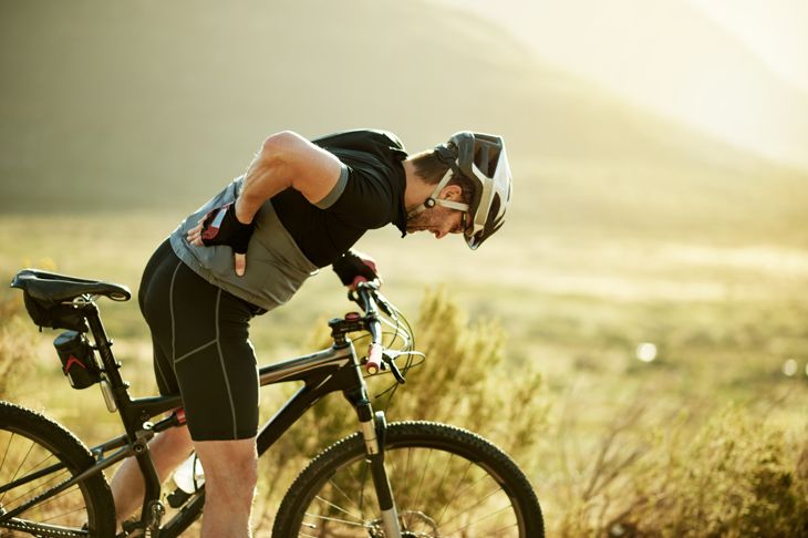 Shot of a mature man experiencing back pain while riding his mountain bike