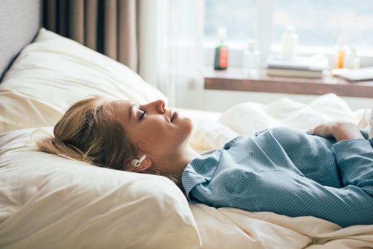 Smiling woman lying in bed and listening to music through her wireless headphones