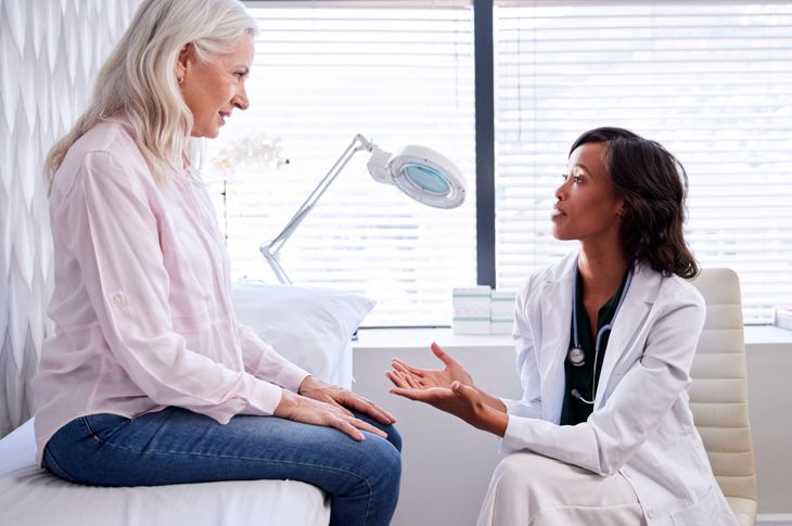 Mature woman consulting with female doctor sitting on examination couch in office