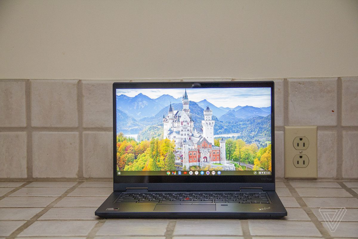 The Lenovo ThinkPad C13 Yoga Chromebook seen from the front on a tile counter.  The screen shows a white castle surrounded by trees with mountains in the background.