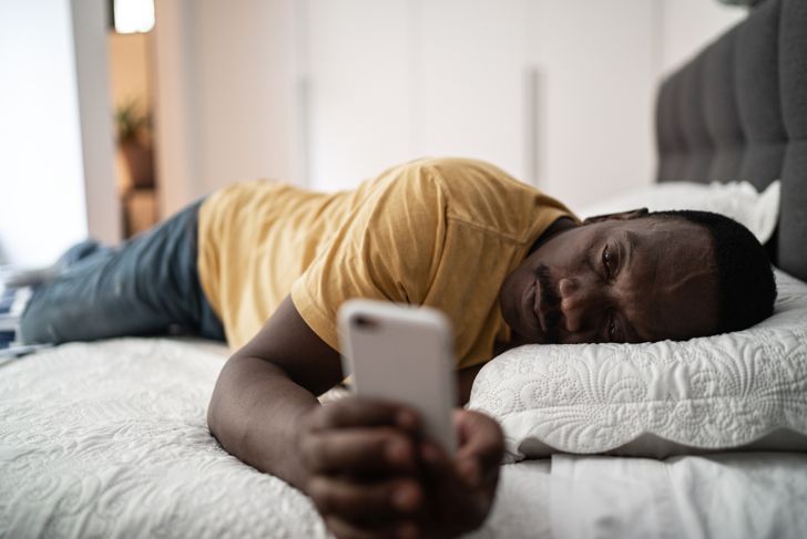 Tired senior man with smartphone lying in bed at home