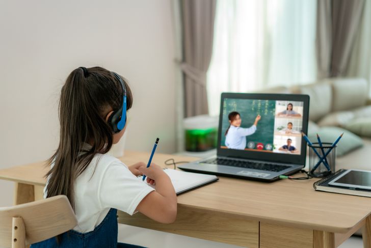 girl learns with teacher and classmates through video conferencing at home