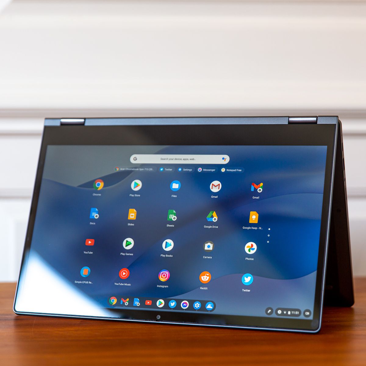 The Lenovo Flex 5 Chromebook in tent mode, tilted to the left.  The screen shows a grid of Chrome OS icons on a blue wavy background.
