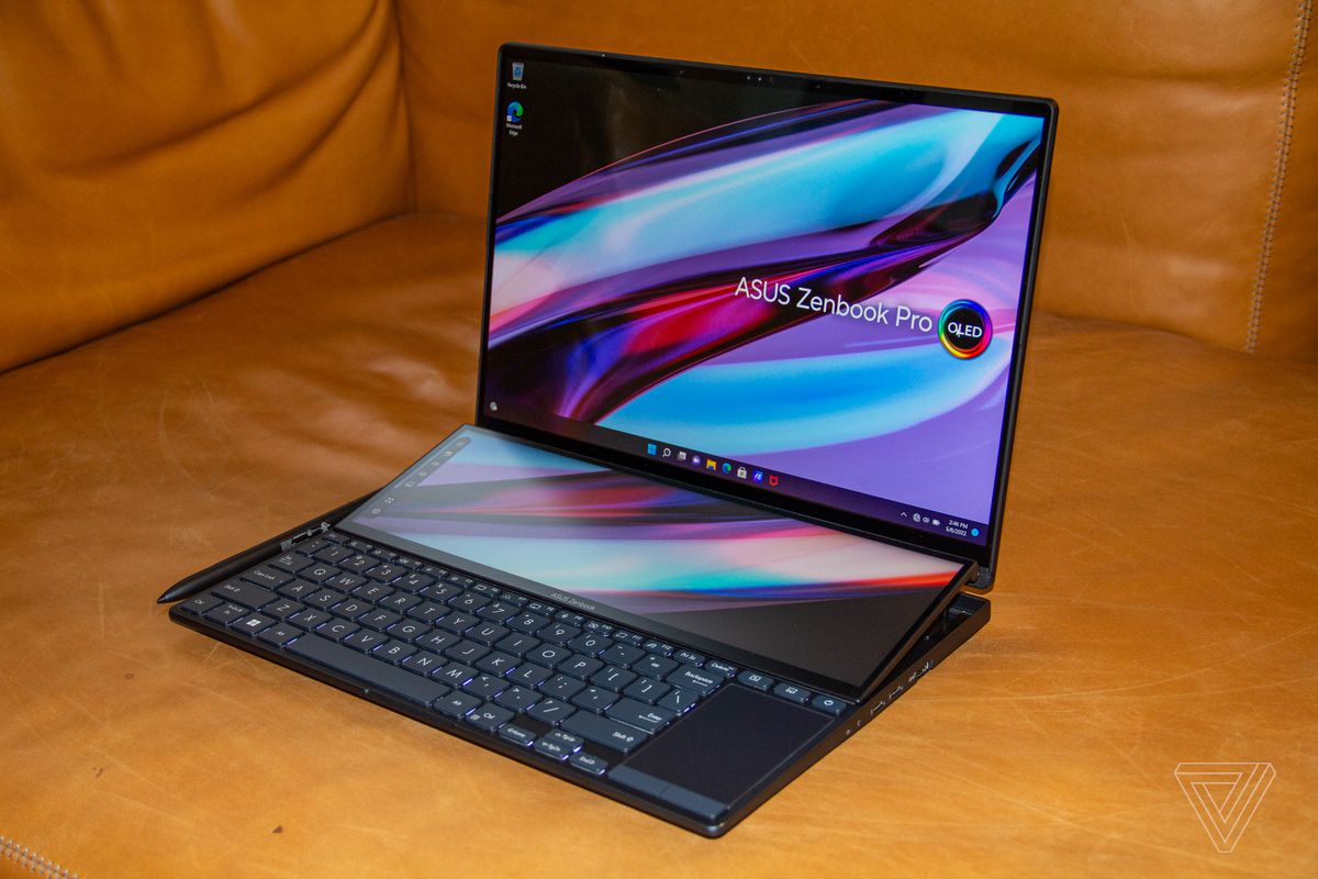 The Asus Zenbook Pro 14 Duo tilted to the left on a brown couch.  Both screens display a multicolored background with the Asus Zenbook Pro OLED logo.