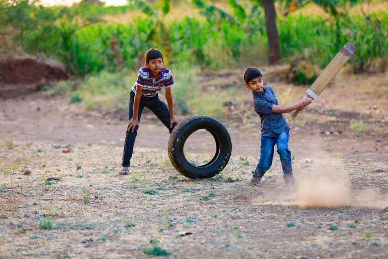 Two boys playing cricket in a rural setting