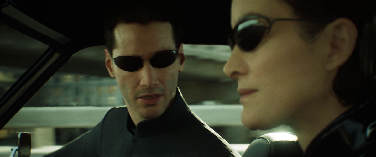 Image of a virtual Neo and Trinity from the Matrix, driving a car with sunglasses on.