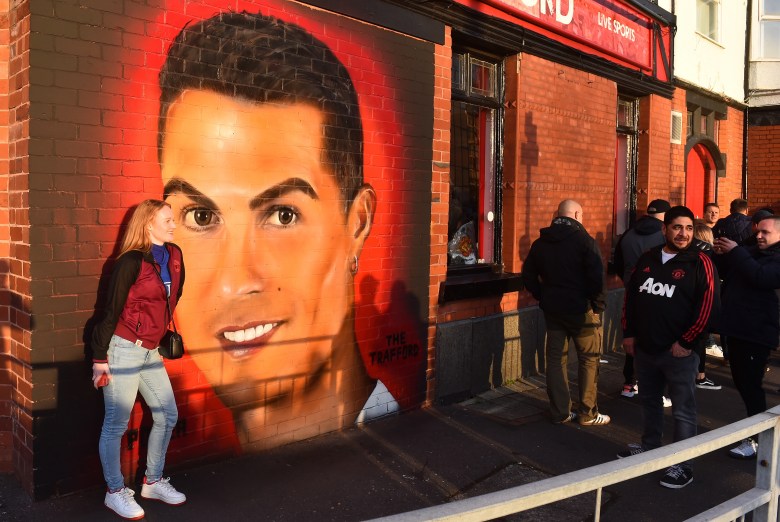 Fans pose and walk past a mural of cristiano ronaldo's face on the wall of a pub outside old trafford stadium