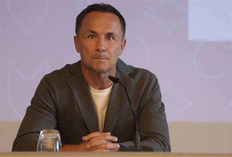 Dennis wise sits in a suit in front of a small microphone.