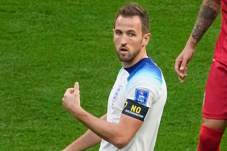A soccer player in a white shirt with a black armband with yellow letters that read: no discrimination.