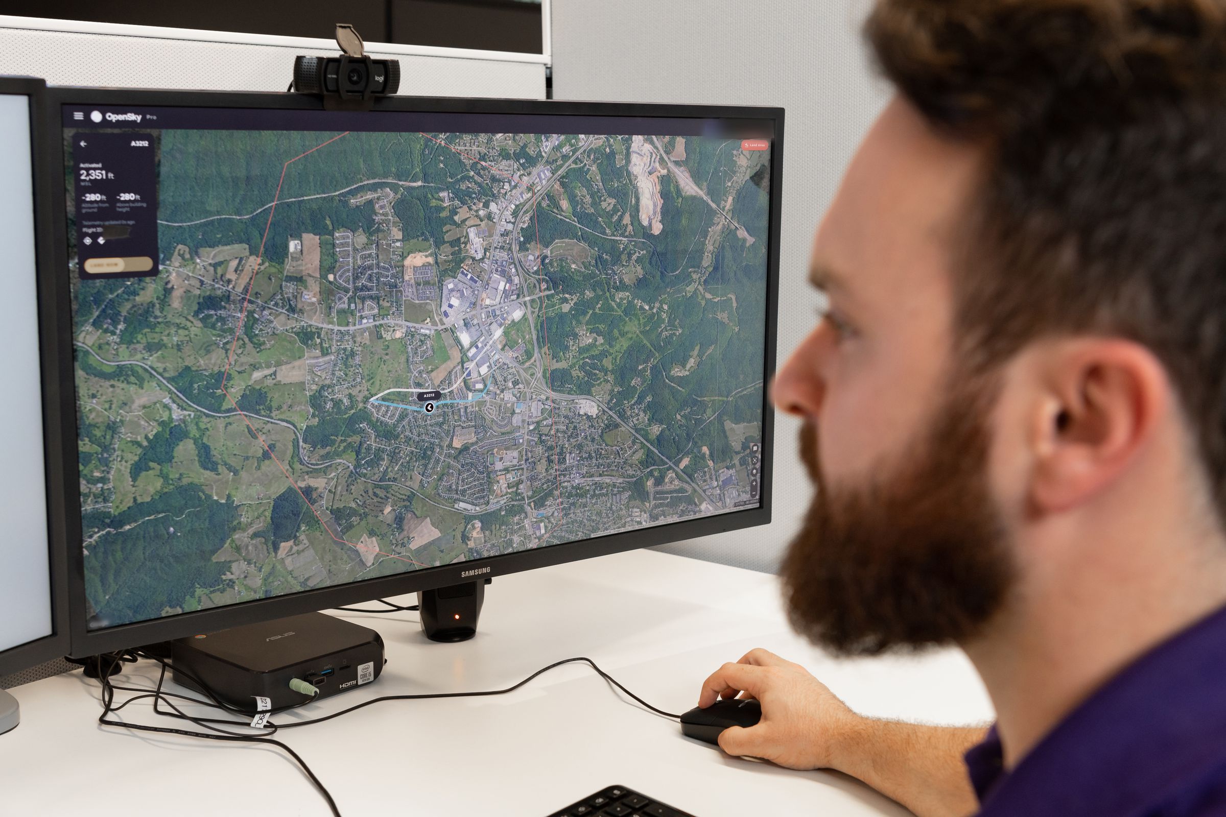 A person with a beard uses a computer with a screen that shows a map with data on the top left.